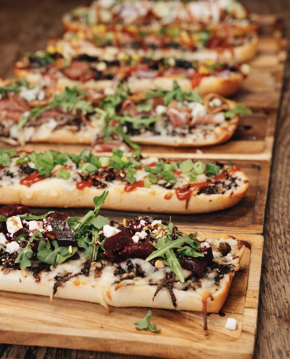 Lineup of fresh zapiekanka open-face baguettes on wooden boards at Spoko, Lincoln Park Chicago